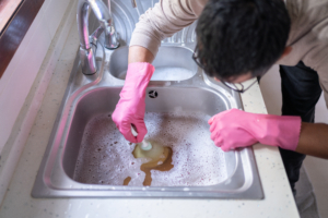Man Using Plunger In Kitchen Sink